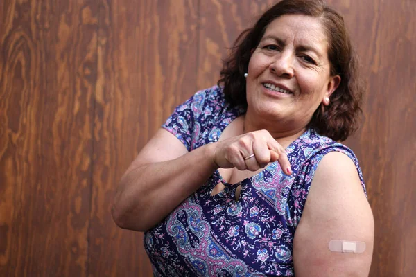 Hispanic old woman shows her arm recently vaccinated against Covid-19 in the new normal for the Coronavirus pandemic