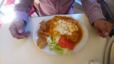Traditional Mexican dish enchiladas which are fried tortillas rolled up filled with chicken with cream, cheese covered in tomato sauce and salad