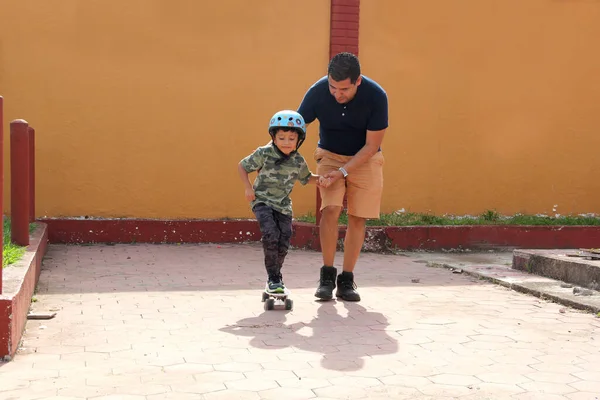 Latin single dad teaches his son to ride a skateboard with a helmet very funny and happy of the achievement of learning something new