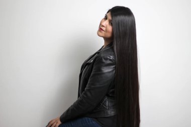 Havada uçuşan uzun düz siyah saçlı Latin yetişkin bir kadın siyah deri ceket giyen ve mutlu.