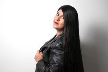 Havada uçuşan uzun düz siyah saçlı Latin yetişkin bir kadın siyah deri ceket giyen ve mutlu.