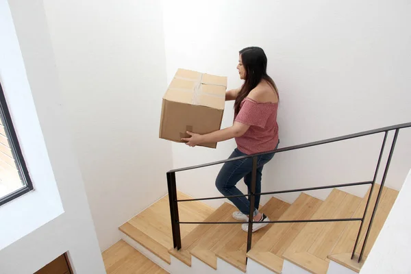 Latin adult woman carries a cardboard box on the stairs of his house during a move opens house that she bought in real estate very happy for the change