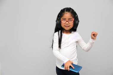 4-year-old brunette Latin girl with glasses listens to music in her headphones connected to her cell phone dances, sings and enjoys the rhythm happy and excited