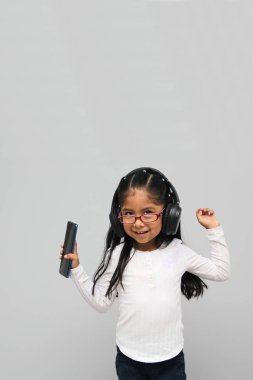 4-year-old brunette Latin girl with glasses listens to music in her headphones connected to her cell phone dances, sings and enjoys the rhythm happy and excited