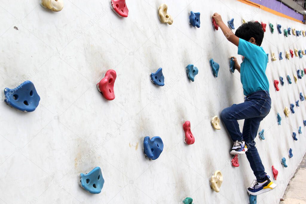 Latin dark-haired male child with blue t-shirt practicing sports wall climbing without fear of heights and exercising