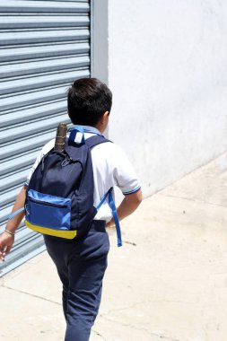 Hispanic male child ready for back to school with uniform and backpack takes his way to go to school healthy and safe