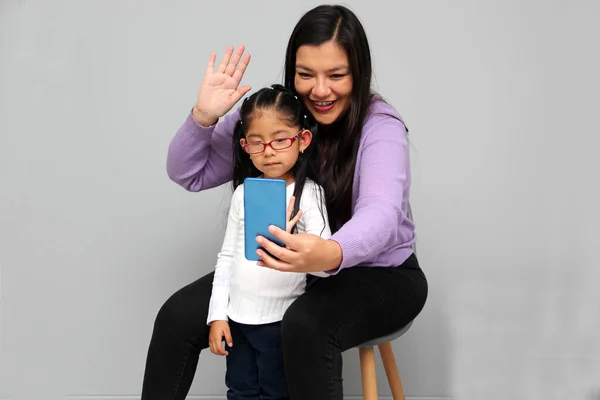 Single divorced Latina mom and daughter use cell phone to video call, take selfies, play video games, and shop online