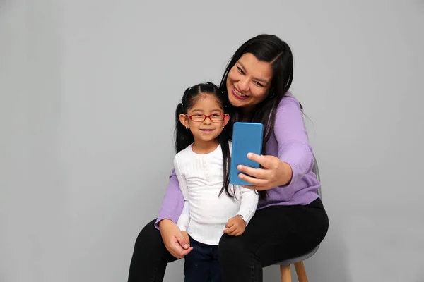 Single divorced Latina mom and daughter use cell phone to video call, take selfies, play video games, and shop online