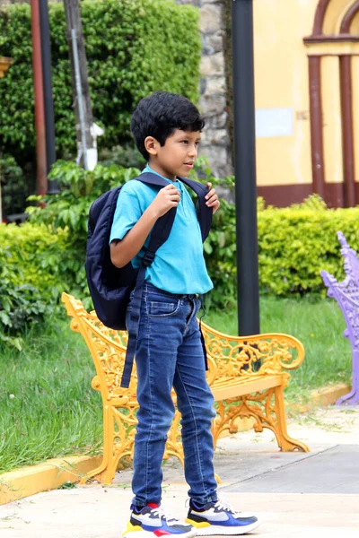 Poor dark-haired 8-year-old Latin boy walks down the street on his way to study back to school with a backpack, the family makes an economic effort in their poverty to buy the books and notebooks