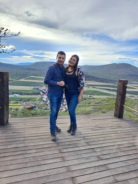 Couple of Latin adult man and woman enjoy the mountainous view of vineyards from a viewpoint you can see the land planted with vines