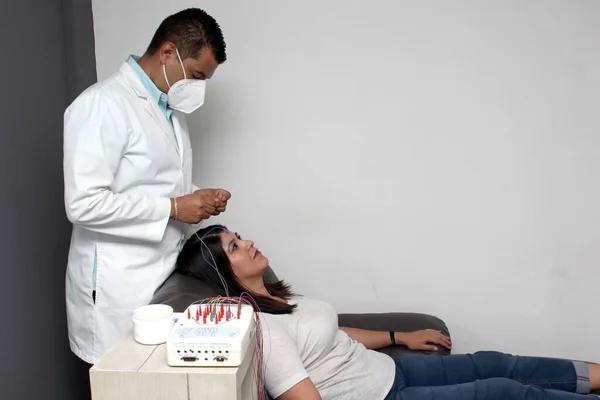 Latin neurologist medical specialist doctor measures the head of his Latin woman patient to stick the electrodes and check the brain activity with an electroencephalogram EEG
