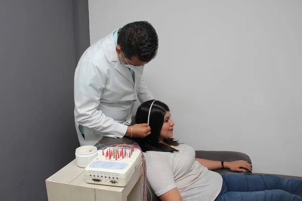 Latin neurologist medical specialist doctor measures the head of his Latin woman patient to stick the electrodes and check the brain activity with an electroencephalogram EEG