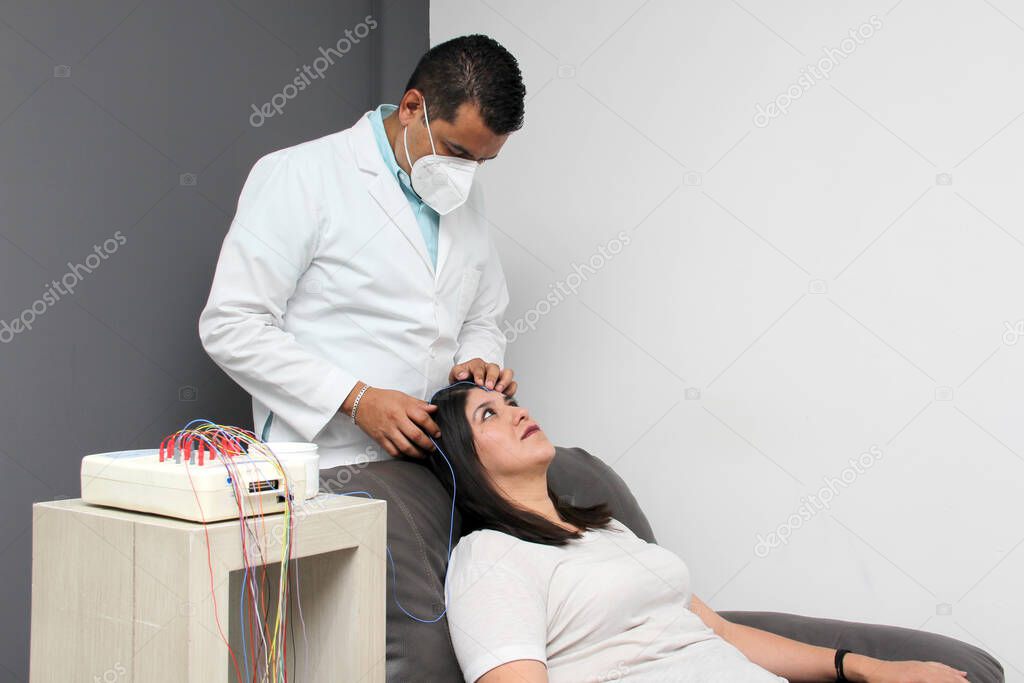 Latin neurologist medical specialist doctor measures the head of his Latin woman patient to stick the electrodes and check the brain activity with an electroencephalogram EEG