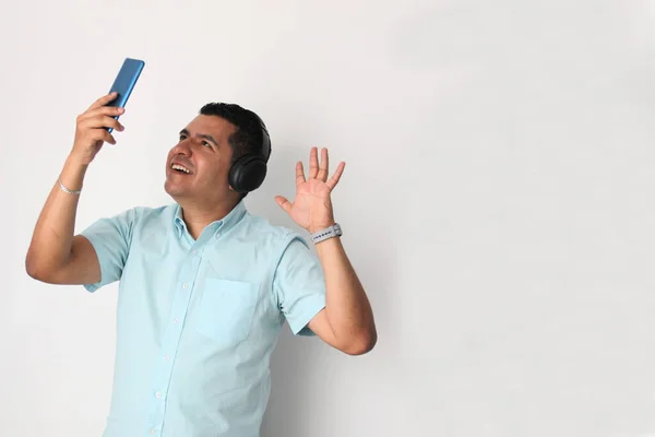Latino adult man uses technology with his cell phone and headphones to listen to music, play video games, make video calls, watch series, and date on the app