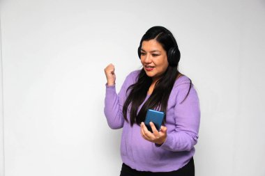 Latino adult woman uses technology with his cell phone and headphones to listen to music, play video games, make video calls, watch series, shopping and date on the app