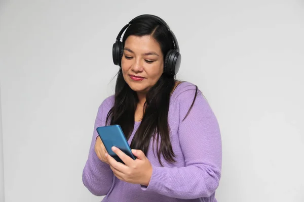 Latino adult woman uses technology with his cell phone and headphones to listen to music, play video games, make video calls, watch series, shopping and date on the app