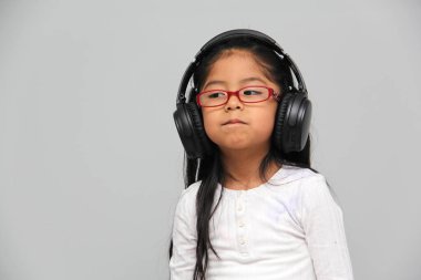 4-year-old brunette Latin girl with glasses listens to music in her headphones connected to her cell phone dances, sings and enjoys the rhythm happy and excited