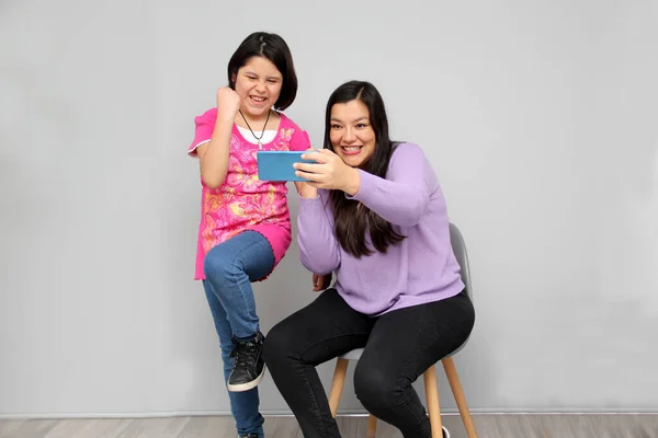 Hispanic Latino mom and daughter play, dance, surprise, enjoy, taking selfies using the cell phone spending quality family time