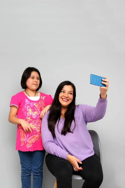 Hispanic Latino mom and daughter play, dance, surprise, enjoy, taking selfies using the cell phone spending quality family time