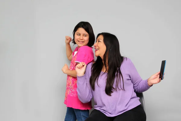 Hispanic Latino mom and daughter play, dance, surprise, enjoy, taking selfies using the cell phone spending quality family time