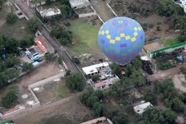 Gündoğumunda renkli sıcak hava balonları bitki örtüsü ve şehir manzarası üzerinde süzülüyor.