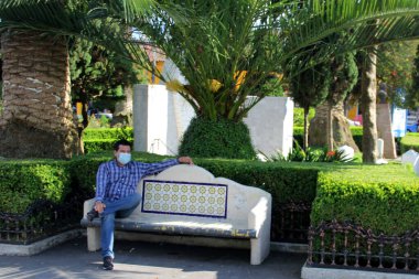 Koruyucu maskeli latin adam park bankında oturuyor. Yeni normal Coffid-19.