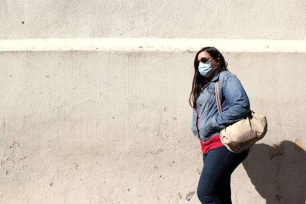 black hair latin woman with protection mask walking in the street with new normality covid-19