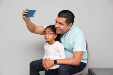 Boşanmış bekar Latin bir baba ve kızı cep telefonuyla video çekiyor, selfie çekiyor, video oyunları oynuyor ve internetten alışveriş yapıyor.