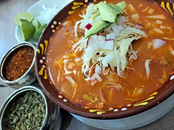Pozole is a traditional soup or stew from Mexican cuisine, with hominy, meat, and can be seasoned and garnished with shredded lettuce, chile peppers, onion, garlic, radishes, avocado, salsa and limes