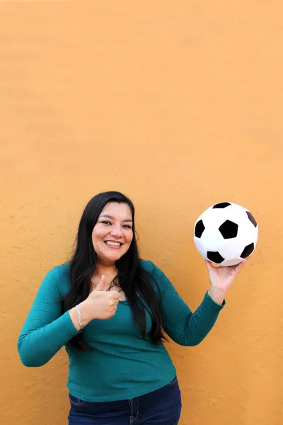 Latino adult woman plays with a soccer ball very excited that she is going to see the World Cup and wants to see her team win