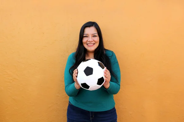 Latino adult woman plays with a soccer ball very excited that she is going to see the World Cup and wants to see her team win