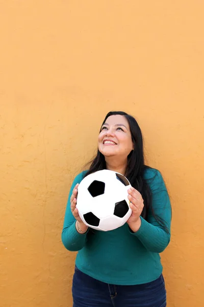 Latino adult woman plays with a soccer ball very excited that she is going to see the World Cup and wants to see her team win