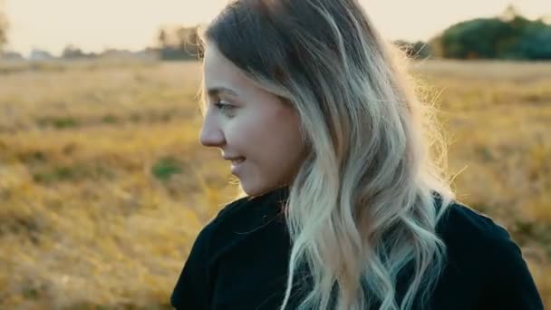 初秋の日没の感情と笑顔の選択的焦点で自然を背景に長い流れるブロンドの髪の美しい少女の感情的な肖像画 — ストック動画
