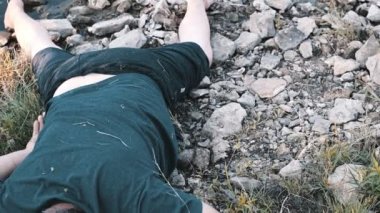 Suda öldürülmüş bir adam, bir ceset, yaşlanmış bir genç adam göl kenarında yatıyor kayaların üzerinde yüzükoyun, kirli bir havuz kenarında bir ceset kararsız bir kamera hareketi renk düzeltmesi.