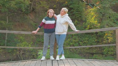 Anne ve kızı köprüde sarılıyor doğada kameraya bakıyor..