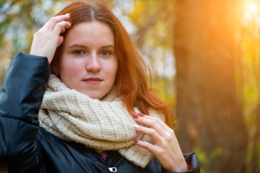 Saçını düzelten ceketli ve atkılı kızıl saçlı gülümseyen bir kızın portresi. Sonbahar doğasına ve parlak güneşe karşı, insani duygular kavramına karşı..