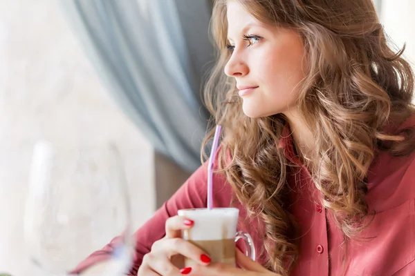 Unga leende kvinna dricker kaffe på ett kafé — Stockfoto