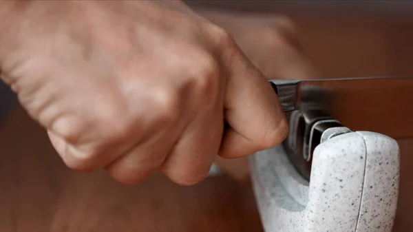 Man manually sharpening kitchen knife in a sharpener.