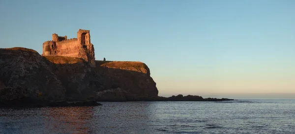 Ruins of an old castle standing on a cliff by the sea at sunset — Fotografia de Stock