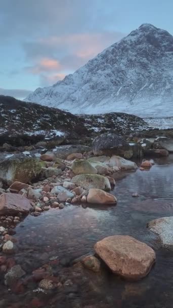 A calm river with stones on the foreground at the foot of a big mountain — Stockvideo