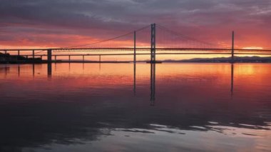 A view of two bridges and the sunset light reflected in the calm sea water. 4k video of a large bridge at sunset. Queensferry Crossing Bridge, Scotland, United Kingdom