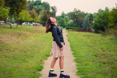 Çok güzel bir genç kız gülümsüyor, gözlerini kapıyor ve yeşil bir parkta başını kaldırıyor.
