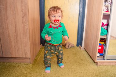 Komik, kızıl saçlı, erkek bebek odasında duruyor.