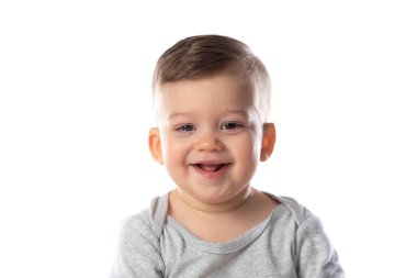 Çıplak ayakla bembeyaz zeminde oturan, vücutlu, gülümseyen bir bebek..