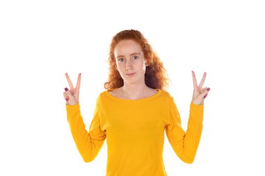 Kızıl saçlı güzel kadın gülümsüyor ve mutlu görünüyor, arkadaş canlısı ve memnun, zafer veya barış işareti yapıyor.