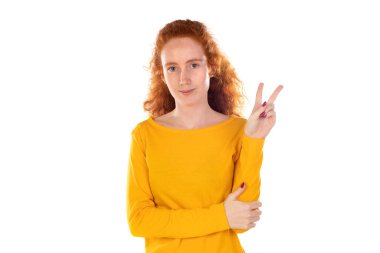 Kızıl saçlı güzel kadın gülümsüyor ve mutlu görünüyor, arkadaş canlısı ve memnun, zafer veya barış işareti yapıyor.