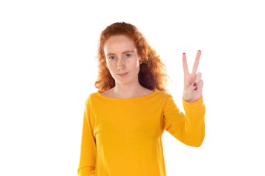 Kızıl saçlı güzel kadın gülümsüyor ve mutlu görünüyor, arkadaş canlısı ve memnun, zafer veya barış işareti yapıyor.