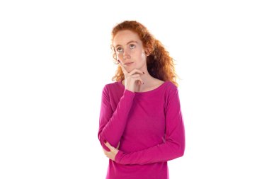 Düşünceli, mutlu bir kadının fotoğrafı, bir şeyler hayal ediyor, dalgalı kızıl doğal saçları var, günlük pembe tişörtler giyiyor, beyaz stüdyo duvarına yaslanıyor, 