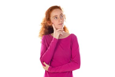 Düşünceli, mutlu bir kadının fotoğrafı, bir şeyler hayal ediyor, dalgalı kızıl doğal saçları var, günlük pembe tişörtler giyiyor, beyaz stüdyo duvarına yaslanıyor, 