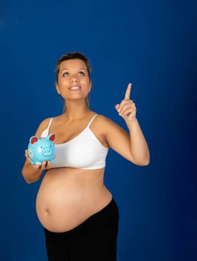 Hamilelik. Mavi arka planda izole edilmiş para kutusu olan mutlu hamile kadın.